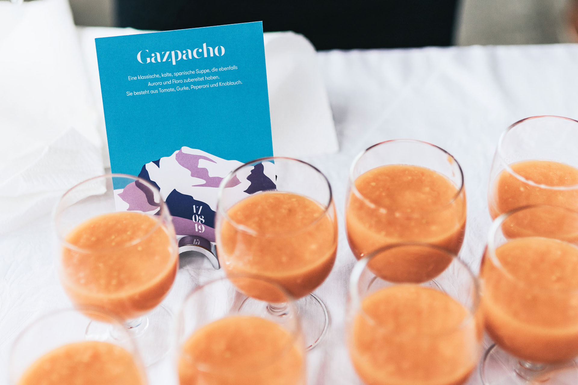 card with e menu item and illustrations on it in front of glasses filled with gazpacho